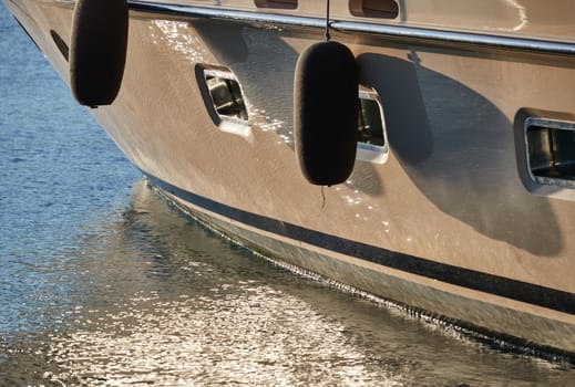 Board of the big boat of gold color, golden reflections of the sun on water at sunset, interesting texture, smooth lines