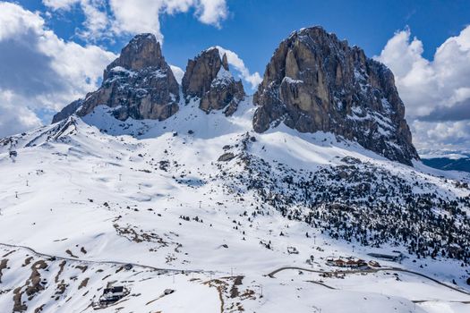 Aerial view of the Dolomites snow-covered mountains in Italy at sunny day, Canazei, drone view point, the twisted road, the blue sky with white clouds, famous place in the world, UNESCO monument, no people