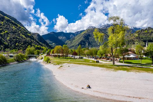 The Improbable aerial landscape of village Molveno, Italy, azure water of lake, The couple sits on a beach, snow covered mountains Dolomites on background, sunny weather, a piers