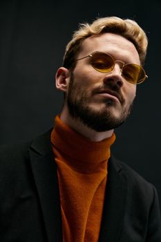 fashionable blond man in a sweater and a jacket on a dark background tilted his head to the side cropped view close-up. High quality photo