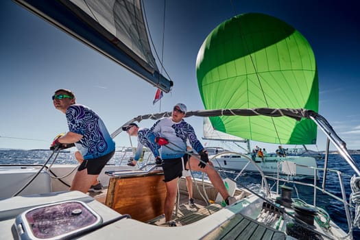 Croatia, Mediterranean Sea, 18 September 2019: The team of sailboat turns off the boat, sailboats compete in a sail regatta, The team works, pulls to a rope, the captain stands behind a steering wheel