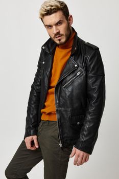 stylish guy in a leather jacket and trousers and in a sweater posing on a light background. High quality photo