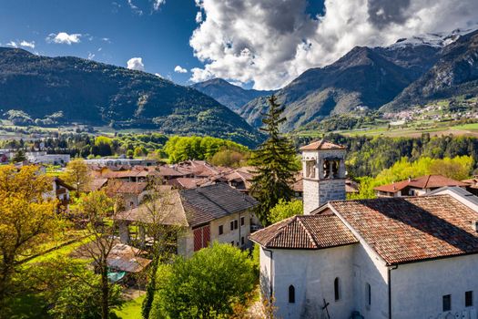 Aerial view of valley with church in Cares, Trentino, green slopes of the mountains of Italy, huge clouds over a valley, Dolomites on background