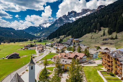 Aerial view of valley with Chalet, green slopes of the mountains of Italy, Trentino, Fontanazzo, huge clouds over a valley, roofs of houses of settlements, green meadows, Dolomites on background, sunny weather