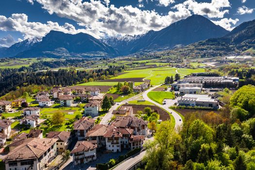 Aerial view of improbable green meadows of Italian Alps, Comano Terme, huge clouds over a valley, roof tops of houses, Dolomites on background, sunshines through clouds, sunny weather