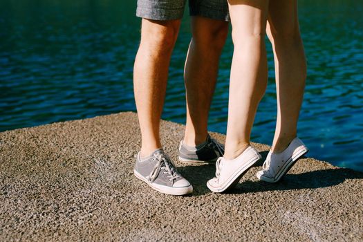 Legs of a man and a woman in sneakers standing hugging each other on the pier close-up, a woman is standing on tiptoe . High quality photo
