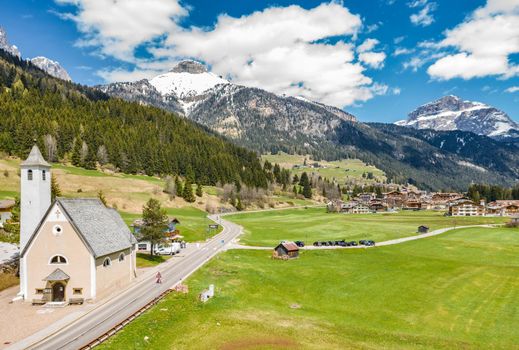 Aerial view of valley with Chalet, green slopes of the mountains of Italy, Trentino, Fontanazzo, huge clouds over a valley, roofs of houses of settlements, green meadows, Dolomites on background, sunny weather