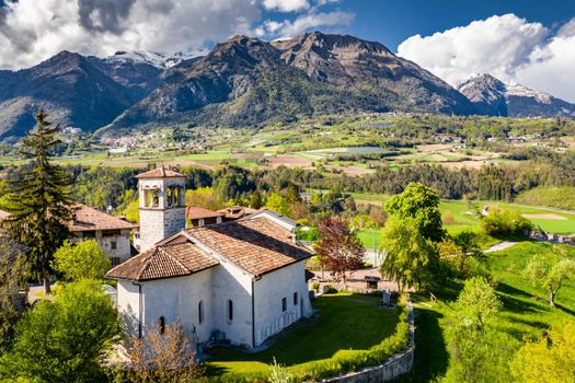 Aerial view of valley with church in Cares, Trentino, green slopes of the mountains of Italy, huge clouds over a valley, Dolomites on background