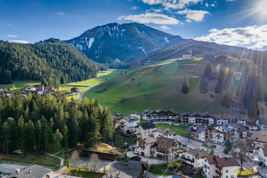 Aerial view of valley and small city with church, green slopes of the mountains of Italy, Trentino, San Martino in Badia, roofs of houses of settlements, green meadows, Dolomites on background, sunset