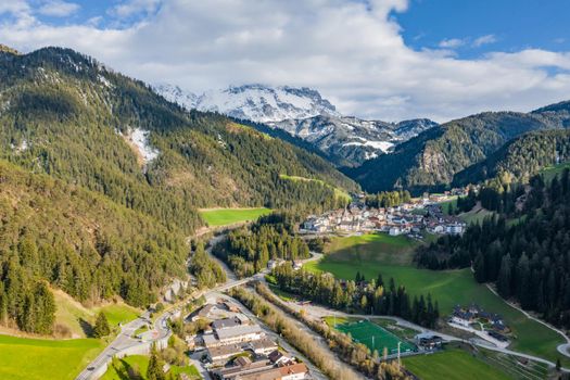 Aerial view of improbable green meadows of Italian Alps, Comano Terme, huge clouds over a valley, roof tops of houses, Dolomites on background, sunshines through clouds, sunny weather