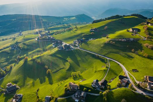 Aerial view of improbable green meadows of the Italian Alps, green slopes of the mountains, Bolzano, huge clouds over a valley, roof tops of houses, Dolomites on background, sunshines through clouds