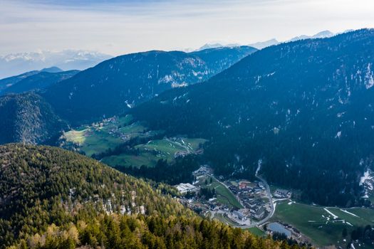 Aerial view of huge valley of the mountains of Italy, Trentino, Slopes with green spruce trees, Dolomites on background, The town in the bottom of a valley