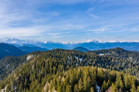 Aerial view of huge valley of the mountains of Italy, Trentino, Slopes with green spruce trees, Dolomites on background, The town in the bottom of a valley