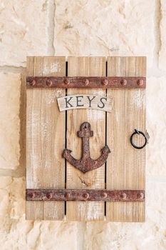 A wooden key box with the inscription Keys and a metal ship anchor hangs on a stone wall
