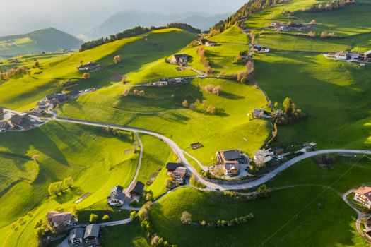 Aerial view of improbable green meadows of the Italian Alps, green slopes of the mountains, Bolzano, huge clouds over a valley, roof tops of houses, Dolomites on background, sunshines through clouds