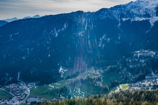 Aerial view of huge valley of the mountains of Italy, Trentino, Slopes with green spruce trees, Dolomites on background, The town in the bottom of a valley