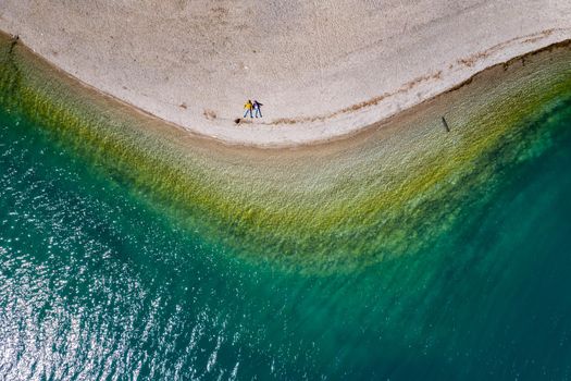 The couple sits on a beach, azure water of lake, The Improbable aerial landscape of coastline, Italy, Dolomites, sunny weather