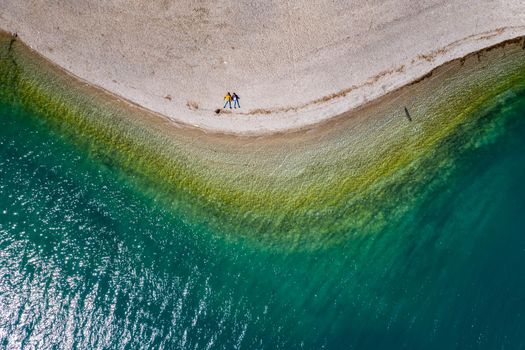 The couple sits on a beach, azure water of lake, The Improbable aerial landscape of coastline, Italy, Dolomites, sunny weather