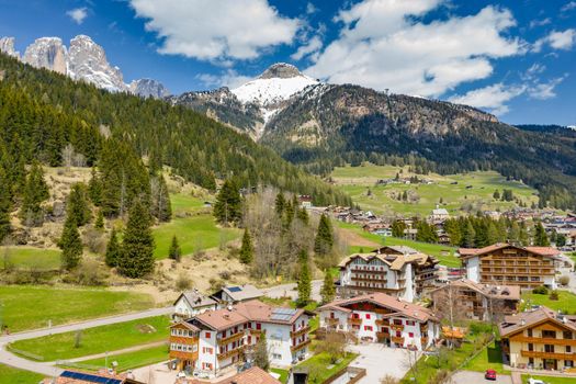 Aerial view of valley with Chalet, green slopes of the mountains of Italy, Trentino, Fontanazzo, huge clouds over a valley, roofs of houses of settlements, green meadows, Dolomites on background, sunny weather