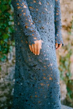 Hands of the woman in stylish blue lace dress standing and walls entwined with ivy, close-up . High quality photo