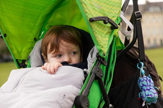 Cute, redhead, blue-eyed baby boy sitting on a green pushchair