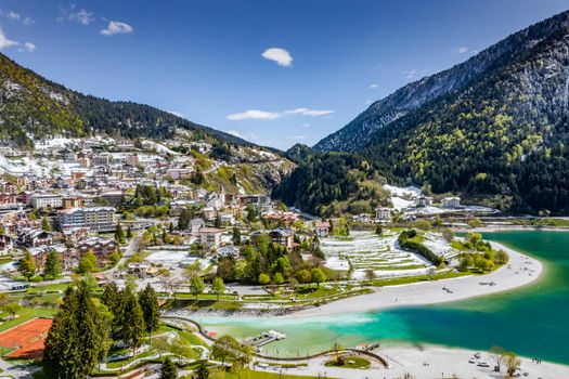 The Improbable aerial landscape of village Molveno, Italy, azure water of lake, empty beach, snow covered mountains Dolomites on background, roof top of chalet, sunny weather, a piers, coastline, slopes