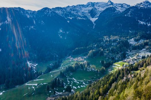 Aerial view of huge valley of the mountains of Italy, Trentino, Slopes with green spruce trees, Dolomites on background, The town in the bottom of a valley