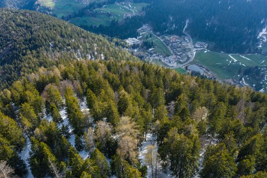 Aerial view of huge valley of the mountains of Italy, Trentino, Slopes with green spruce trees, Dolomites on background, The town in the bottom of a valley