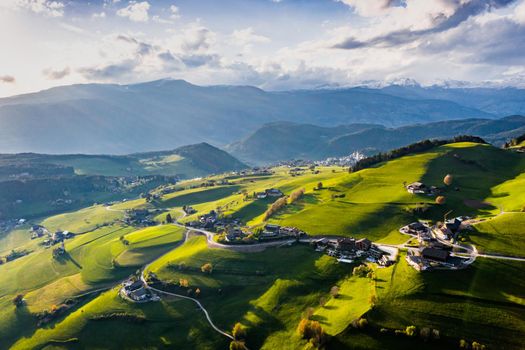 Aerial view of improbable green meadows of the Italian Alps, green slopes of the mountains, Bolzano, huge clouds over a valley, roof tops of houses, Dolomites on background, sunshines through clouds