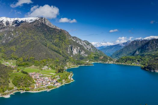 The Improbable aerial landscape of village Molveno, Italy, azure water of lake, empty beach, snow covered mountains Dolomites on background, roof top of chalet, sunny weather, a piers, coastline, slopes