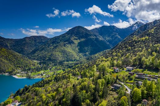 The Improbable aerial landscape of village Molveno, Italy, azure water of lake, empty beach, snow covered mountains Dolomites on background, roof top of chalet, sunny weather, a piers, coastline, slopes