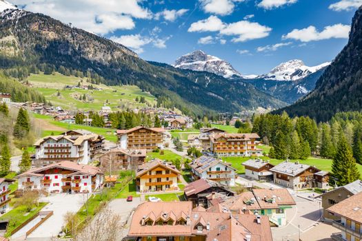 Aerial view of valley with Chalet, green slopes of the mountains of Italy, Trentino, Fontanazzo, huge clouds over a valley, roofs of houses of settlements, green meadows, Dolomites on background, sunny weather