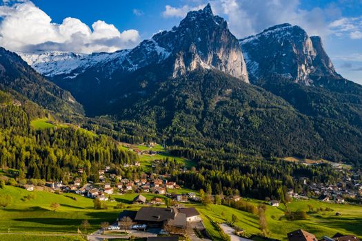 Aerial view of improbable green meadows of the Italian Alps, green slopes of the mountains, Bolzano, huge clouds over a valley, roof tops of houses, Dolomites on background, sunshines through clouds