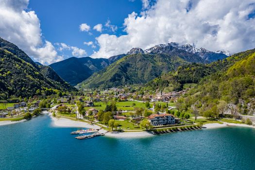 The Improbable aerial landscape of village Molveno, Italy, azure water of lake, empty beach, snow covered mountains Dolomites on background, roof top of chalet, sunny weather, a piers, coastline, slopes