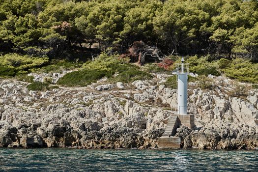 Small lighthouse on the island, Stone coast, sunny weather, green trees