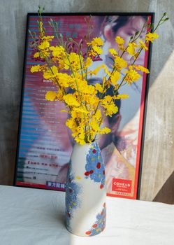Yellow flowers in Handmade ceramic vase and with Classic chinese poster movie frame with old ruins cement wall. Home decor, Selective focus.