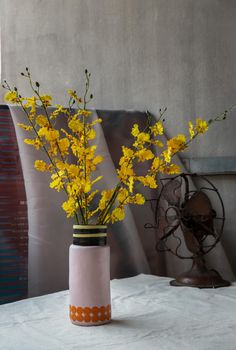 Bouquet of yellow flowers in Handmade ceramic vase and Vintage fan on white textured table cloth with old cement wall. Home decor, No focus, specifically.