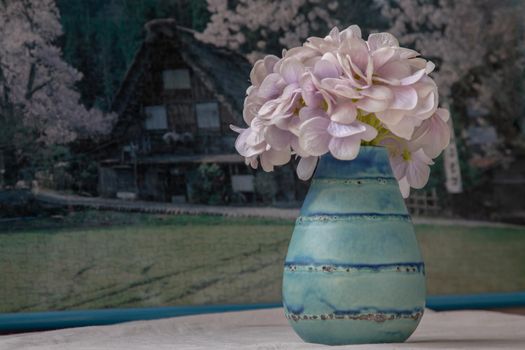Bangkok, Thailand - Feb 06, 2021 : Bouquet of purple flowers in Blue handmade ceramic vase on white textured table cloth in front of Beautiful scenery wallpaper. Home decor, Selective focus.