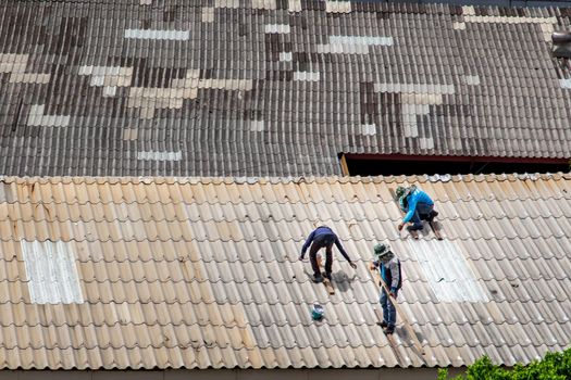 Bangkok, Thailand - 13 Jun 2020 : Three handyman workers repairing tiles on the damaged factory roof.