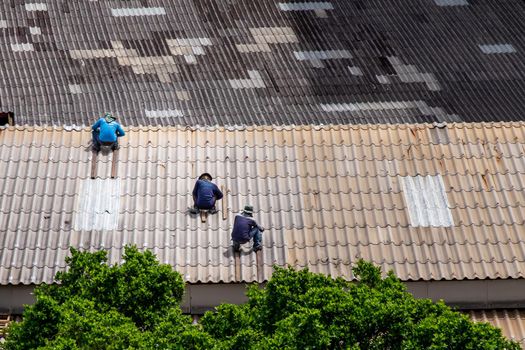 Bangkok, Thailand - 13 Jun 2020 : Three handyman workers repairing tiles on the damaged factory roof.