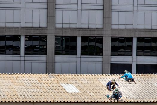 Bangkok, Thailand - 13 Jun 2020 : Three handyman workers repairing tiles on the damaged factory roof.