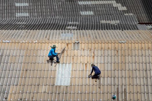 Bangkok, Thailand - 13 Jun 2020 : Two handyman workers repairing tiles on the damaged factory roof.