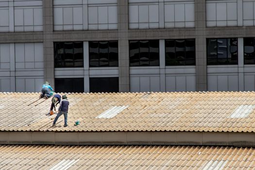 Bangkok, Thailand - 13 Jun 2020 : Three handyman workers repairing tiles on the damaged factory roof.