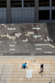 Bangkok, Thailand - 13 Jun 2020 : Two handyman workers repairing tiles on the damaged factory roof.