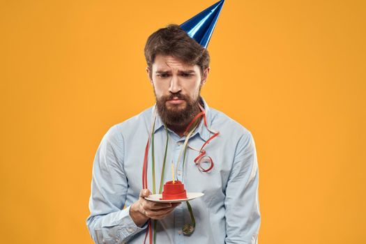 Cheerful man with a cake on a yellow background birthday holidays cap on his head. High quality photo