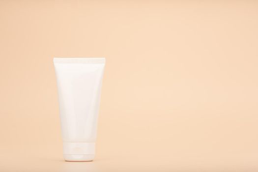 White cream tube against beige background with copy space. Concept of beauty products for skin care. Skin cream, mask scrub or exfoliation product