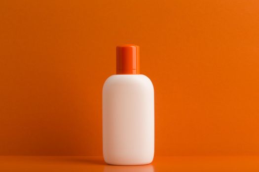 Cosmetic bottle with sunscreen cream or lotion against orange background. Concept of safe tanning and summer skin care on vacation