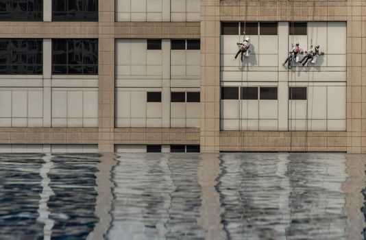 Group of workers cleaning windows service on high rise office building with reflection from swimming pool. Selective focus.