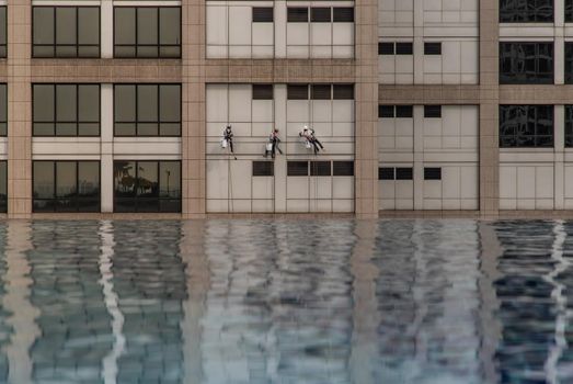 Group of workers cleaning windows service on high rise office building with reflection from swimming pool. Selective focus.