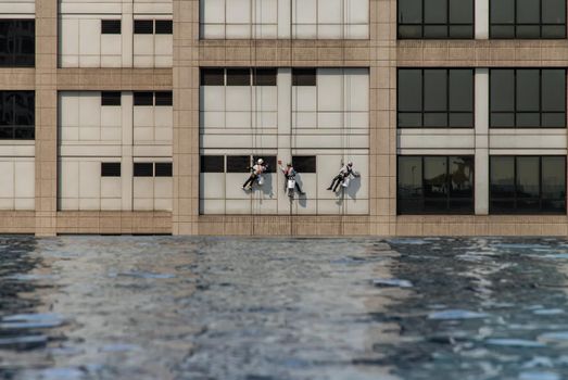 Group of workers cleaning windows service on high rise office building with reflection from swimming pool. Selective focus.